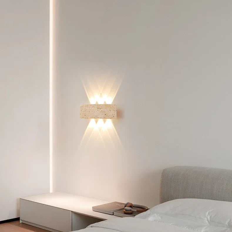 Aure stone wall light creating a quiet warm glow on a bedroom wall