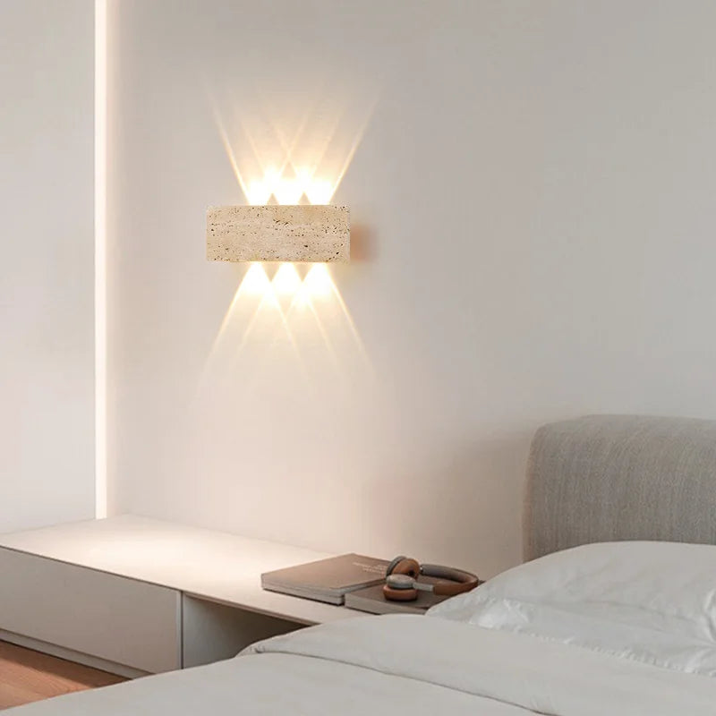 Aure stone wall light creating soft warm illumination beside a modern bed