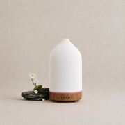 Noctis ceramic essential oil diffuser with a soft white body, warm wood base, and small flower